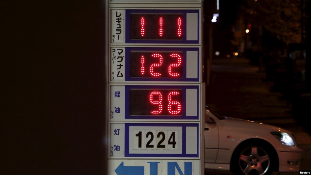 FILE - A car passes behind a board posting oil prices at a service station in Tokyo, Japan, Dec. 16, 2015.