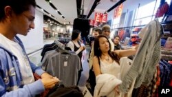 In this Wednesday, Dec. 12, 2012, photo, Lana Nguyen, right, holds up a shirt while helping friend Chris Ghiathi, left, shop in an H&M store, in Atlanta.