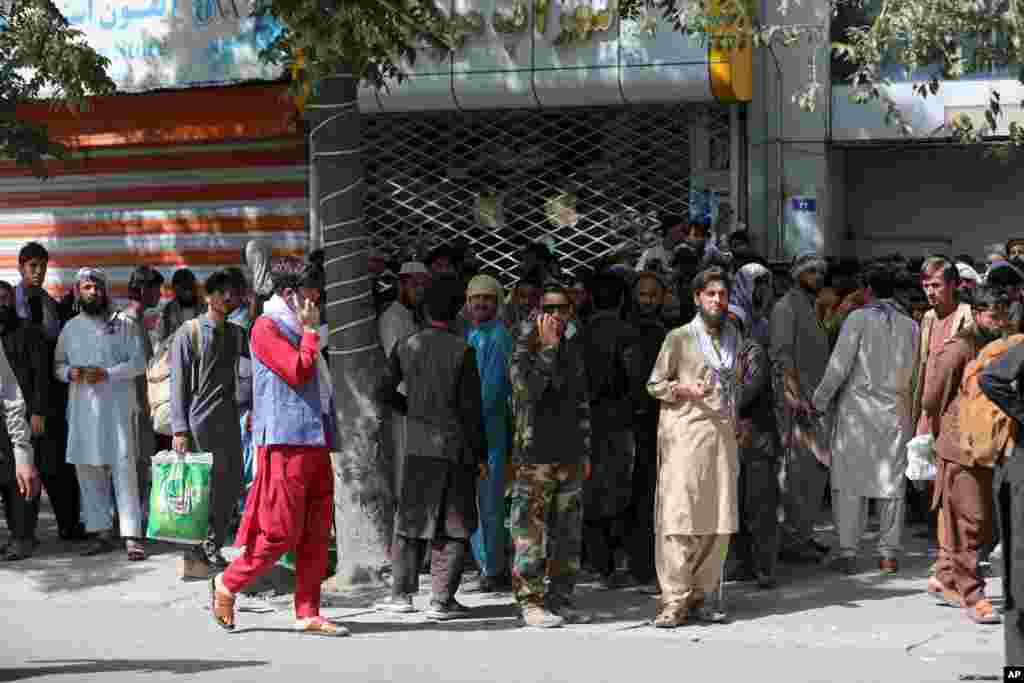 Afghans wait in long lines for hours to withdraw money, in front of Kabul Bank, in Kabul, Aug. 15, 2021.