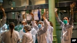 Health workers react as people applaud from their houses in support of the medical staff that are working on the COVID-19 virus outbreak at the main gate of the Hospital Clinic in Barcelona, Spain, March 26, 2020. 