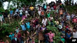 Para pemuda muslim Rohingya berdiri di lereng bukit dan merentangkan tangan mereka untuk menerima makanan yang didistribusikan di dekat kamp pengungsi Balukhali di Cox's Bazar, Bangladesh, Rabu, 20 September 2017. (AP Photo/Bernat Armangue)