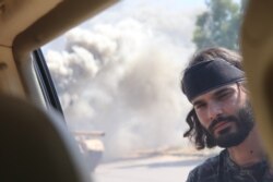 Mohammad Basheer, a fighter for Tripoli's forces, is seen next to a burning tank in Tripoli, Libya, July 7, 2019. (H.Murdock/VOA)