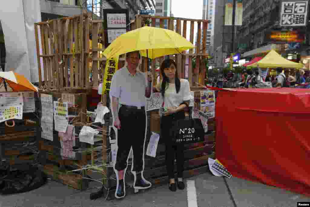 A woman poses with a cutout of Chinese President Xi Jinping and a yellow umbrella, symbol of the Occupy Central civil disobedience movement, in front of a barricade set up by pro-democracy demonstrators in the Mongkok shopping district, Hong Kong, Oct. 28, 2014. 