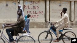FILE - Two boys ride their bicycles past a sign reading "Stop killing Muslims Army" on a wall in Kano, Nigeria, April 8, 2016. 