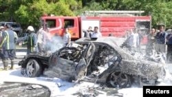 Petugas pemadam kebakaran Suriah memadamkan mobil yang terbakar pasca serangan bom di distrik Mazzeh, Damaskus, Senin (29/4). PM Suriah lolos dari serangan bom mobil ini.