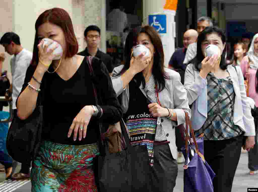 Women cover their faces with masks as haze shrouds Singapore&#39;s central business district.
