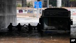 Passengers are silhouetted as they wade through high water after evacuating a bus stuck in a flooded underpass in southern Athens, Oct. 14, 2021. 