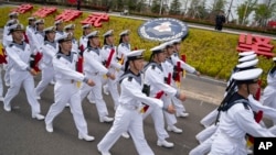 在中國山東省青島市舉行的西太平洋海軍研討會開幕前一天，在為外國記者安排的參觀活動中，水兵們從中國人民解放軍海軍潛艇學院的徽章前走過。 （2024年4月21日）