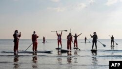 Members and friends of a Cypriot surfing club, dressed as Santa Claus to celebrate the holidays, set out to sea on stand up paddle (SUP) boards at Makenzy beach, in the southern city of Larnaca.