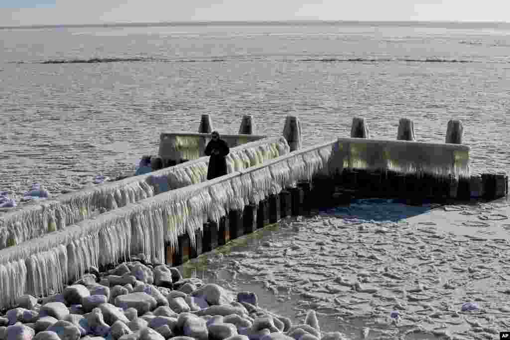 A woman takes pictures of icicles on a jetty at the Afsluitdijk, a dike separating the IJsselmeer inland sea, and the Wadden Sea, Netherlands.