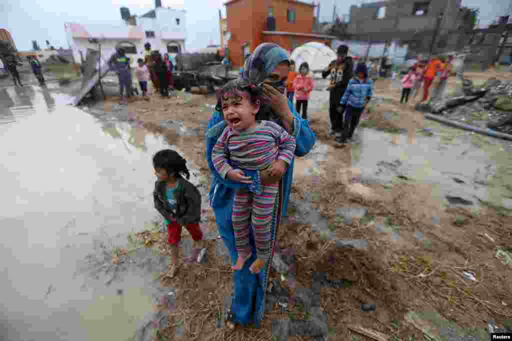 Seorang perempuan Palestina menggendong putrinya setelah hujan menyebabkan banjir di rumahnya. Para saksi mengatakan rumah perempuan itu rusak akibat gempuran Israel dalam perang 50 hari pertengahan tahun lalu di Jalur Gaza.