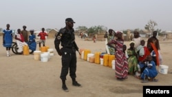 A Cameroonian police officer stands next to people waiting for water at the Minawao refugee camp for Nigerians who fled Boko Haram attacks in Minawao, Cameroon, March 15, 2016.