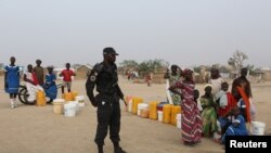   DOSSIER - A Cameroonian policeman stands beside people waiting for him Water at the Minawao refugee camp. Boko Haram attacks in Minawao, Cameroon, March 15, 2016. 