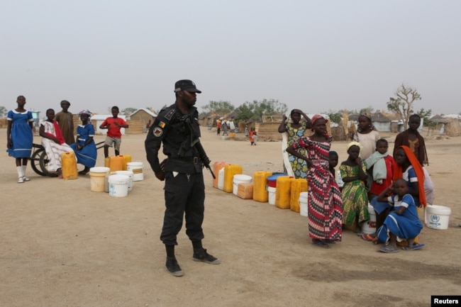 FILE - A Cameroonian police officer stands next to people waiting for water at the Minawao refugee camp for Nigerians who fled Boko Haram attacks in Minawao, Cameroon, March 15, 2016.