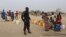 A Cameroonian police officer stands next to people waiting for water at the Minawao refugee camp for Nigerians who fled Boko Haram attacks in Minawao, Cameroon, March 15, 2016.
