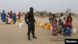 FILE - A Cameroonian police officer stands next to people waiting for water at the Minawao refugee camp for Nigerians who fled Boko Haram attacks in Minawao, Cameroon, March 15, 2016.