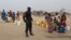 FILE - A Cameroonian police officer stands next to people waiting for water at the Minawao refugee camp for Nigerians who fled Boko Haram attacks in Minawao, Cameroon, March 15, 2016.