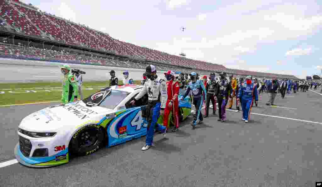 NASCAR drivers Kyle Busch, left, and Corey LaJoie, right, join other drivers and crews as they push the car of Bubba Wallace to the front of the field prior to the start of the NASCAR Cup Series auto race at the Talladega Superspeedway in Talladega, Alabama, June 22, 2020.