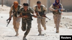 FILE - Kurdish fighters from the People's Protection Units (YPG) run in a street in Raqqa, Syria, July 3, 2017.