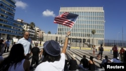 FILE - A woman waves a U.S flag in front of the U.S. Interests Section in Havana, July 20, 2015.