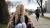 FILE - Colleen Curtin, who says she is suffering from health issues that she has not been able to get diagnosed by testing due to the COVID-19 pandemic, sits in her wheelchair for a portrait along a path in Madison, Wisconsin, April 17, 2020.