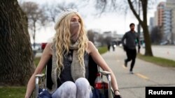 FILE - Colleen Curtin, who says she is suffering from health issues that she has not been able to get diagnosed by testing due to the COVID-19 pandemic, sits in her wheelchair for a portrait along a path in Madison, Wisconsin, April 17, 2020.