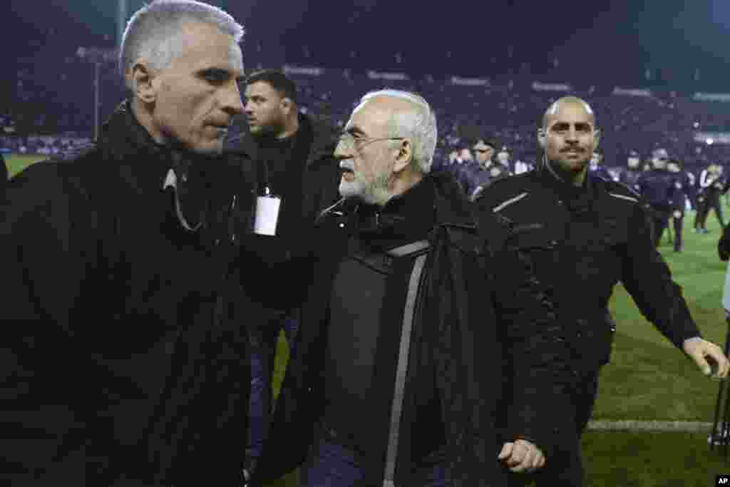 Mai kungiyar PAOK, Ivan Savvidis, rataye da bindiga a kunkuminsa, tare da masu gadinsa, a lokacin da ya kutsa cikin filin wasa a karawarsu da AEK Athens ranar lahadai a birnin Thessaloniki. Sau biyu Savvidis yana kutsawa cikin filin a lokacin wasa. Jami'an AEK sun yi zargin cewa Savvidis yayi barazana ga alkalin wasan a kutsawarsa ta farko, kafin masu gadinsa su janye shi. A karo na biyu an ga bindiga a rataye a kunkuminsa.(InTime Sports via AP)