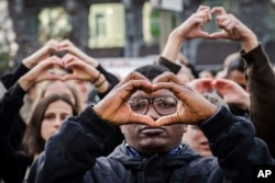 People make the shape of a heart with their hands as they stand for a moment of silence at the Bourse during the one-year anniversary for Brussels attacks victims in Brussels, March 22, 2017.