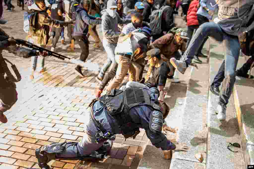 The flash of an exploding stun grenade is seen as a student from the University of Witwatersrand jumps on a falling policeman while another policeman fires rubber bullets from his rifle during a mass demonstration on campus in Johannesburg. Authorities tried to re-open the prestigious Wits University after weeks of demonstrations.