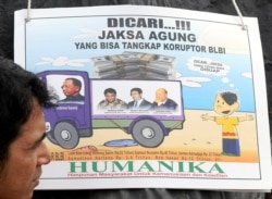 Seorang pengunjuk rasa berdiri di samping sebuah plakat yang menggambarkan Sjamsul Nursalim, Anthony Salim dan ayahnya Sudono Salim -beberapa konglomerat Indonesia yang memiliki hubungan dekat dengan mendiang mantan presiden Suharto, selama protes di luar