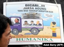 Seorang pengunjuk rasa berdiri di samping sebuah plakat yang menggambarkan Sjamsul Nursalim, Anthony Salim dan ayahnya Sudono Salim -beberapa konglomerat Indonesia yang memiliki hubungan dekat dengan mendiang mantan presiden Suharto, selama protes di luar