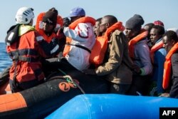 A group of 47 migrants is helped by a Sea-Watch 3 crew member, left, during their transfer from a rescued inflatable boat onto a Sea-Watch 3 RHIB (Rigid Hull Inflatable Boat) during a rescue operation by the Sea-Watch 3 off Libya's coasts, Jan. 19, 2019.