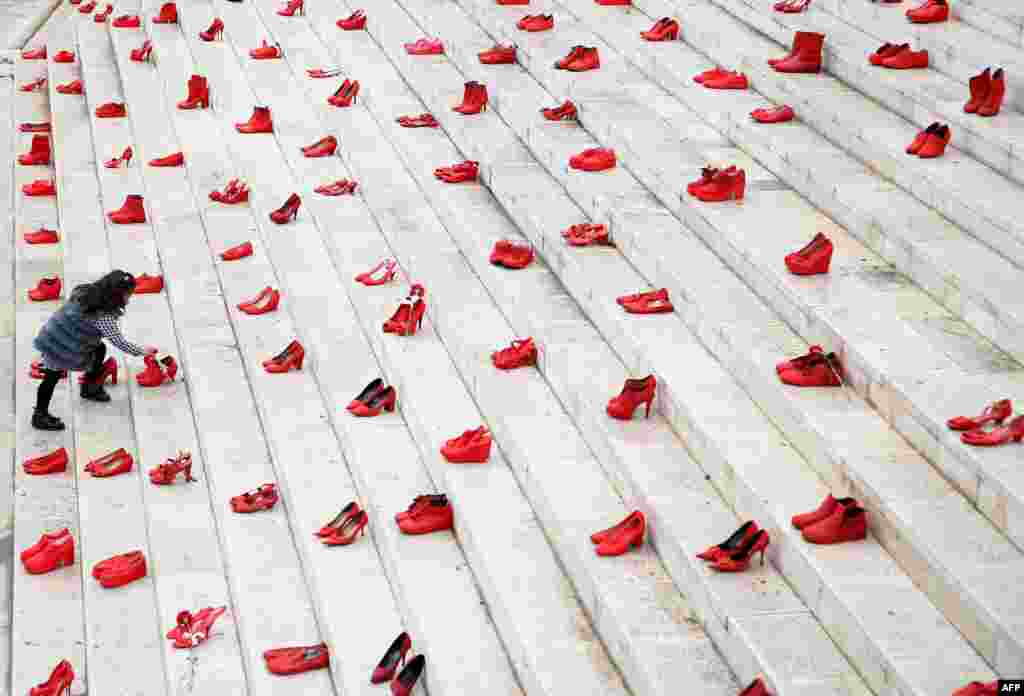 A girl puts flowers at an installation of women's red shoes displayed on a staircase, as a symbol to denounce violence against women, at Durresi main square in Tirana, Albania, on International Women's Day.