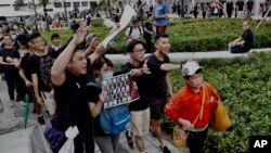  Protesters walk behind a mainland Chinese tourists, holding a card with their demands including "Withdrawal of extradition bill" and "Real elections" during a march in Hong Kong, July 7, 2019.