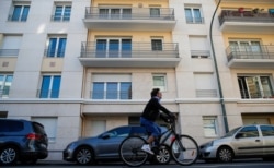 FILE - A man rides a bicycle past an apartment building where Rwanda genocide suspect Felicien Kabuga was arrested in Asnieres-sur-Seine near Paris, France, May 16, 2020.