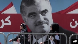 Lebanese women pass by a giant portrait of slain Lebanese Prime Minister Rafik Hariri near his grave, in downtown Beirut, Lebanon, June 30, 2011.