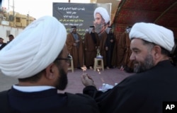 Iraqi Shiite clerics,foreground, attend a symbolic funeral for Sheik Nimr al-Nimr, seen in background photo, a prominent opposition Shiite cleric convicted of terrorism charges and executed by Saudi Arabia, in Basra, Iraq, Jan. 3, 2016.