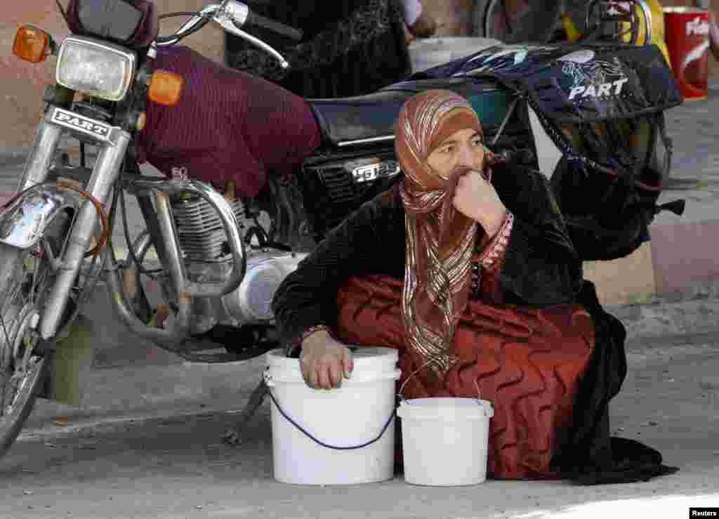 A woman squats next to her buckets as she waits for her turn to receive a free meal from a soup kitchen in the city of Raqqa, eastern Syria.