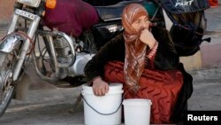 A woman squats next to her buckets as she waits for her turn to receive a free meal from a soup kitchen in the city of Raqqa, eastern Syria, Oct. 7, 2013.