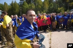 Seorang tawanan perang Ukraina yang dibalut bendera nasional tersenyum setelah pertukaran tawanan di lokasi yang dirahasiakan di Ukraina. (Foto: via AP)