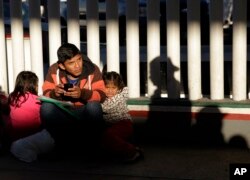 A migrant who did not give his name looks on with his children as they wait to hear if their number is called to apply for asylum in the United States, at the border Friday, Jan. 25, 2019, in Tijuana, Mexico.
