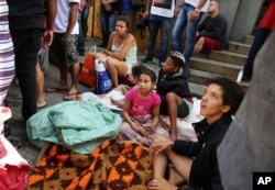 Displaced occupants of a collapsed building sit on the sidewalk in Sao Paulo, Brazil, May 1, 2018. The building collapsed as firefighters worked to put out the flames.