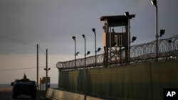 FILE - A U.S. soldier stands in the turret of a vehicle with a machine gun, left, as a guard looks on from a tower at the Guantanamo Bay prison in Cuba.