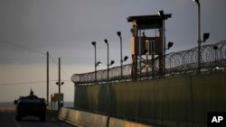 FILE - A U.S. soldier stands in the turret of a vehicle with a machine gun, left, as a guard looks out from a tower at the Guantanamo Bay prison in Cuba, March 30, 2010.