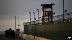 FILE - A U.S. soldier stands in the turret of a vehicle with a machine gun, left, as a guard looks out from a tower at the Guantanamo Bay prison in Cuba, March 30, 2010.