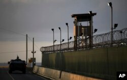 FILE - A U.S. soldier stands in the turret of a vehicle with a machine gun, left, as a guard looks out from a tower at the Guantanamo Bay prison in Cuba, March 30, 2010.