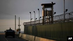 FILE - A U.S. soldier stands in the turret of a vehicle with a machine gun, left, as a guard looks out from a tower at the Guantanamo Bay prison in Cuba, March 30, 2010.