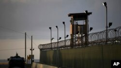 FILE - A U.S. soldier stands in the turret of a vehicle with a machine gun, left, as a guard looks out from a tower at the Guantanamo Bay prison in Cuba, March 30, 2010.