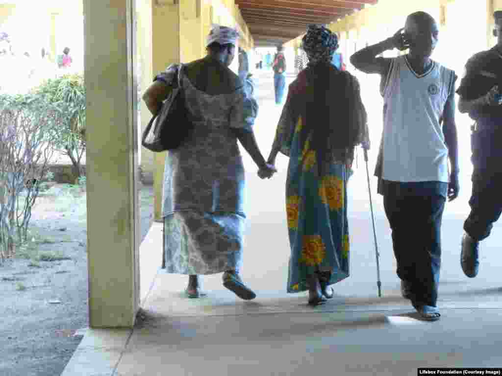 Family members walk hand in hand, supported by crutch, towards the operating theater block.