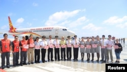 FILE - Crew members pose for pictures in front of a plane of Hainan Airlines as the plane landed at a new airport China built on Subi Reef of the Spratlys, South China Sea, July 13, 2016.